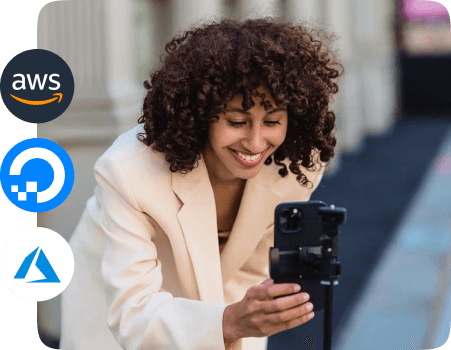 A concept of cloud hosting for MVP apps highlighting a person with obscured facial features is capturing a photo or video using a smartphone mounted on a stabilizer, with logos of AWS, DigitalOcean, and Azure floating nearby.