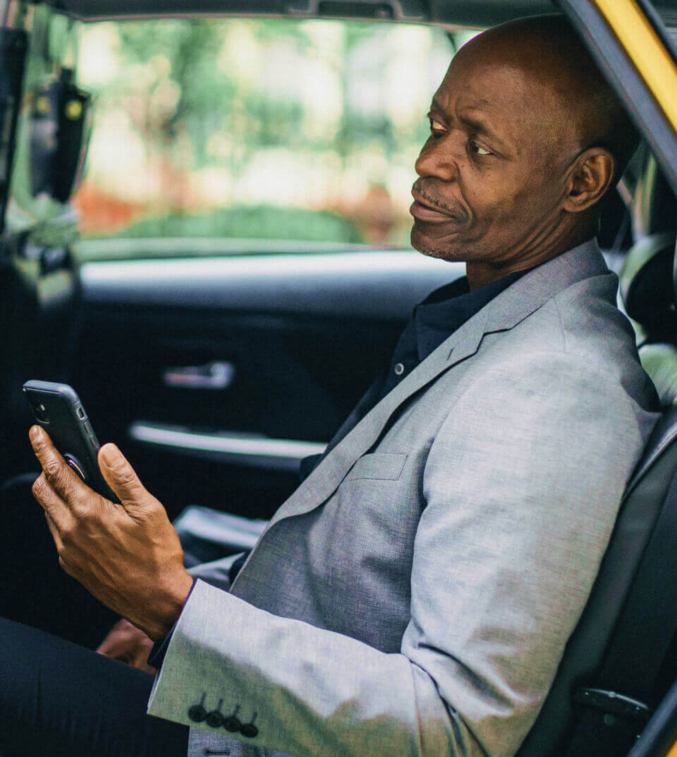 A man is sitting in the back seat of a car, holding a phone in his left hand