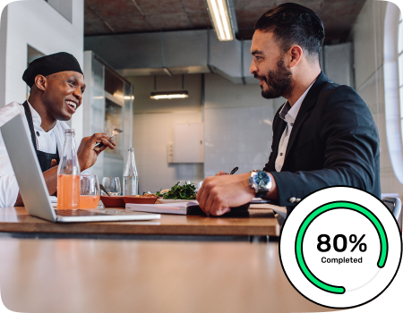 A restaurant entrepreneur talking with his chef having a laptop, diary and drinks on the table